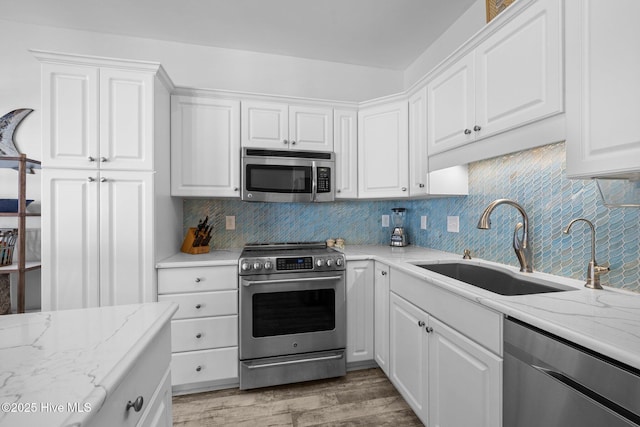 kitchen with appliances with stainless steel finishes, white cabinets, light wood-type flooring, a sink, and decorative backsplash