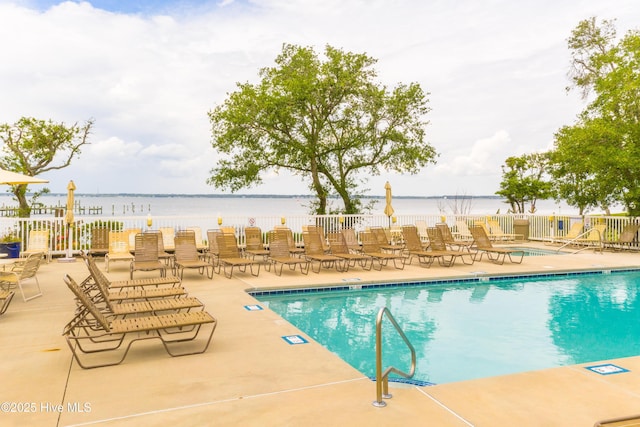 community pool with fence, a patio area, and a water view