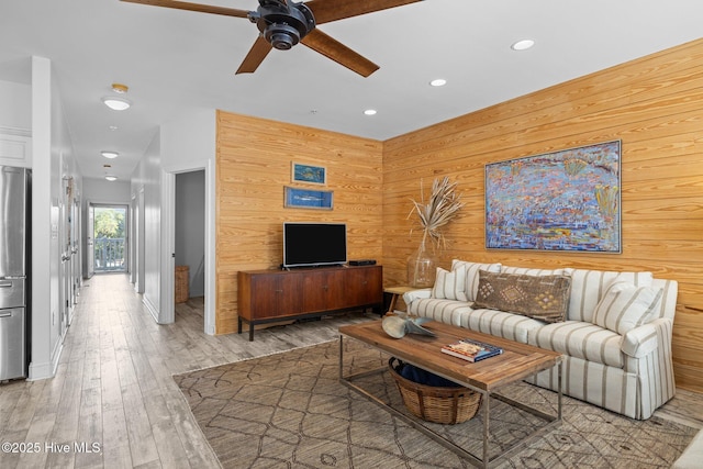living area with a ceiling fan, recessed lighting, light wood finished floors, and wood walls