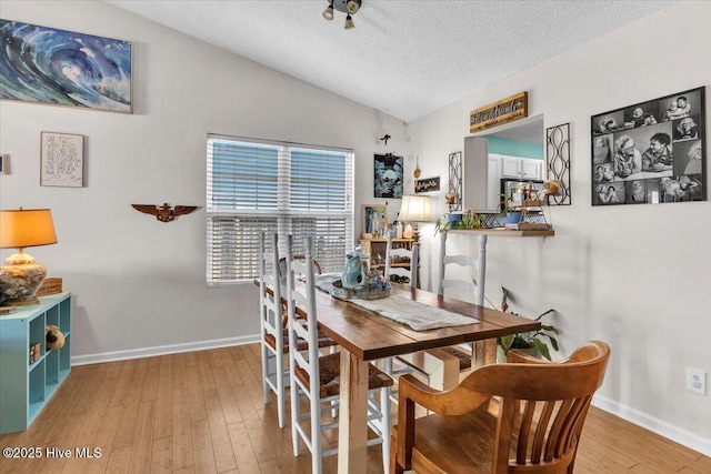 dining room featuring wood finished floors, baseboards, a textured ceiling, and lofted ceiling