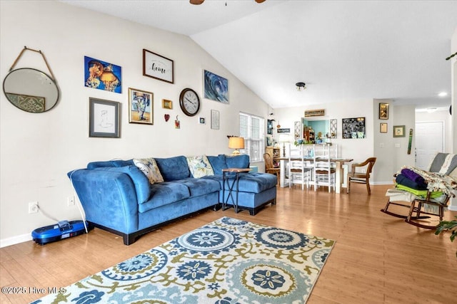 living area with baseboards, ceiling fan, wood finished floors, and vaulted ceiling