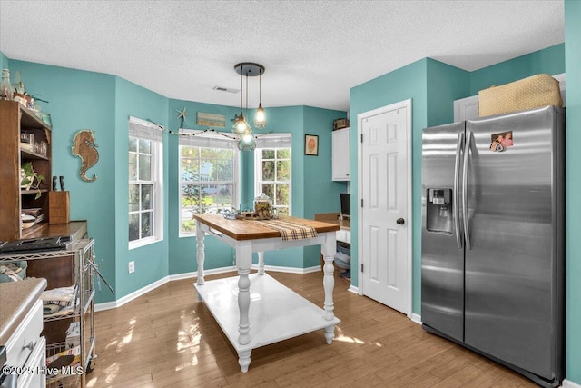 kitchen with stainless steel fridge, light wood-style floors, a textured ceiling, and visible vents