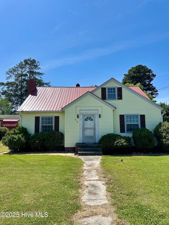 view of front facade with a chimney, a front yard, and metal roof