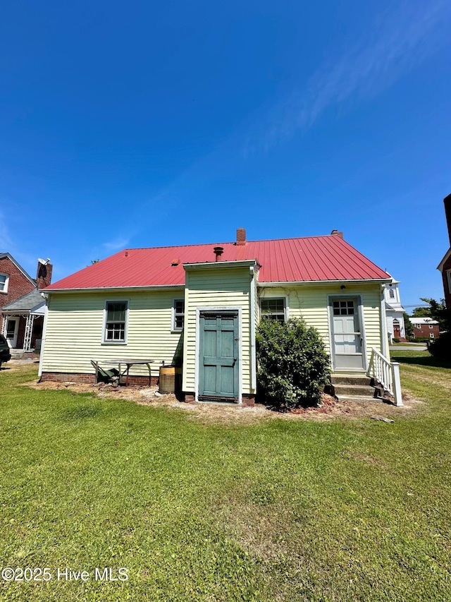rear view of house featuring a lawn, a chimney, entry steps, and metal roof