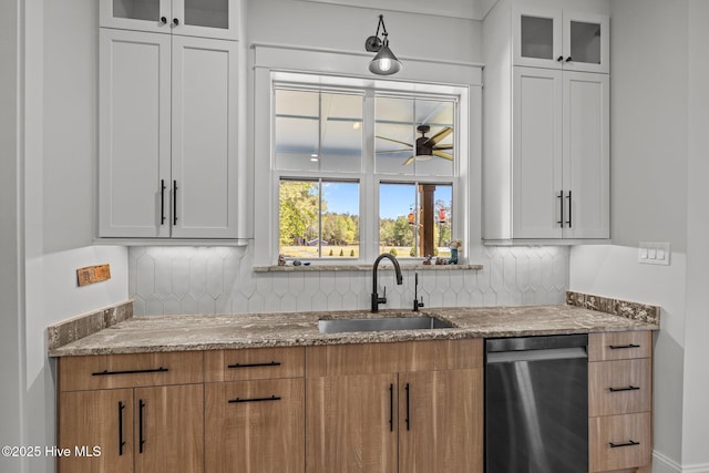 kitchen featuring backsplash, a ceiling fan, dishwasher, a sink, and stone countertops