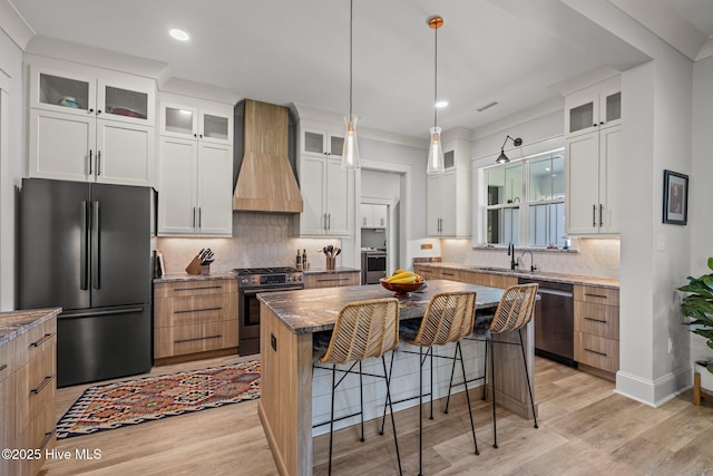 kitchen featuring a kitchen breakfast bar, appliances with stainless steel finishes, light wood finished floors, and premium range hood