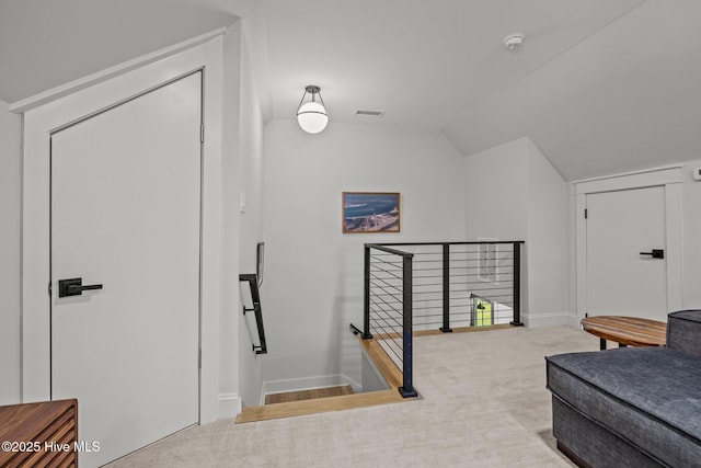 interior space with carpet flooring, visible vents, an upstairs landing, and lofted ceiling