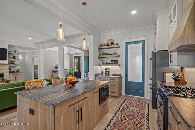 kitchen with wall chimney range hood, light wood-type flooring, black appliances, dark stone counters, and ornamental molding