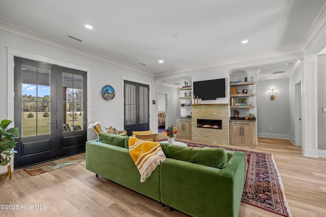 living room featuring crown molding, visible vents, a lit fireplace, french doors, and light wood finished floors