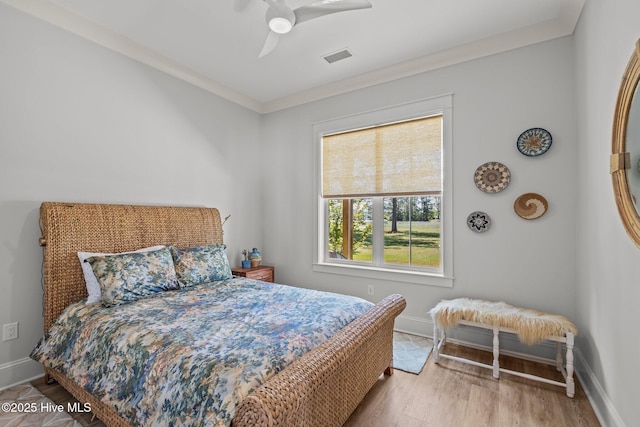 bedroom featuring a ceiling fan, visible vents, wood finished floors, baseboards, and ornamental molding