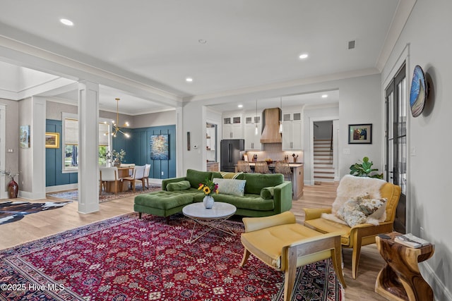 living area featuring visible vents, ornamental molding, stairs, decorative columns, and light wood-style flooring