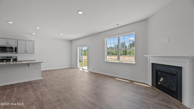 unfurnished living room featuring visible vents, wood finished floors, a fireplace, baseboards, and recessed lighting
