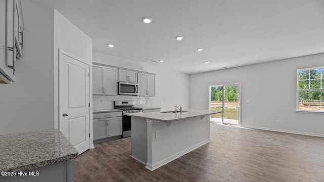 kitchen featuring light stone countertops, a sink, stainless steel appliances, dark wood-type flooring, and backsplash