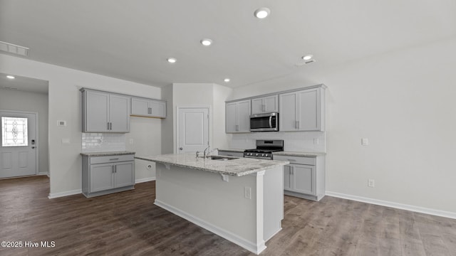 kitchen with appliances with stainless steel finishes, baseboards, tasteful backsplash, gray cabinetry, and a center island with sink