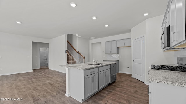 kitchen with appliances with stainless steel finishes, tasteful backsplash, light stone countertops, a center island with sink, and a sink