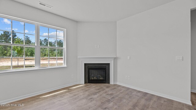 unfurnished living room with plenty of natural light, a glass covered fireplace, wood finished floors, and visible vents
