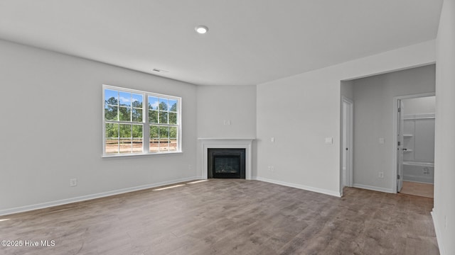 unfurnished living room with a glass covered fireplace, baseboards, wood finished floors, and visible vents