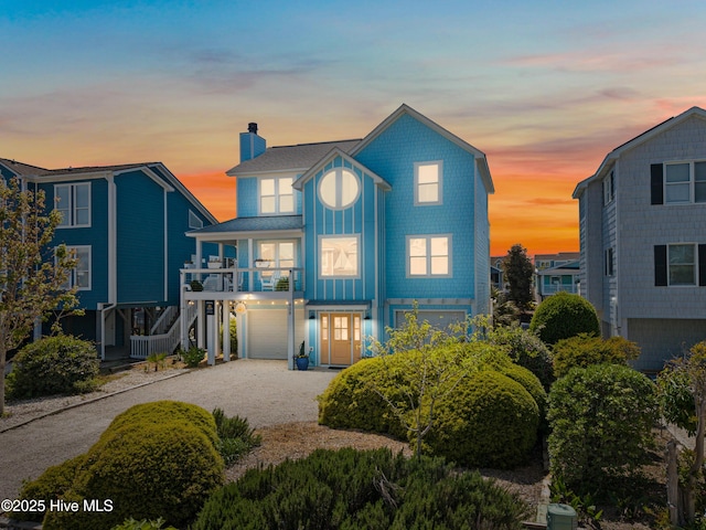 408 Dolphin St, Sunset Beach, NC 28468 - coastal home with roof with shingles, an attached garage, a chimney, a balcony, and gravel driveway