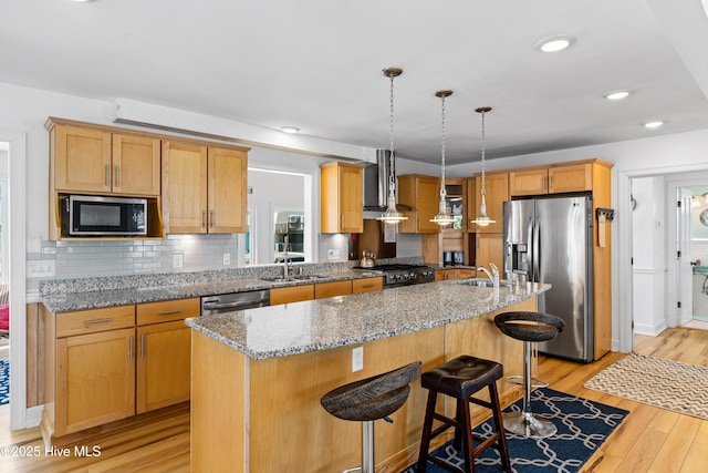 408 Dolphin St, Sunset Beach, NC 28468 - kitchen featuring appliances with stainless steel finishes, a sink, light wood finished floors, wall chimney exhaust hood, and a center island with sink