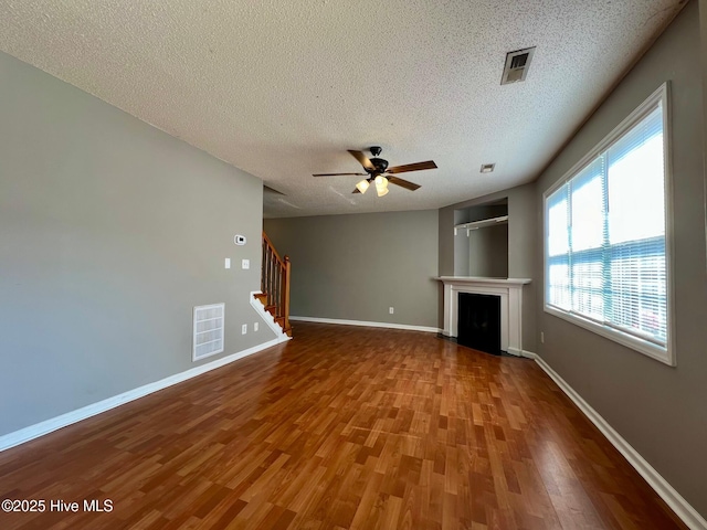 unfurnished living room featuring wood finished floors, stairway, ceiling fan, a textured ceiling, and a fireplace with flush hearth