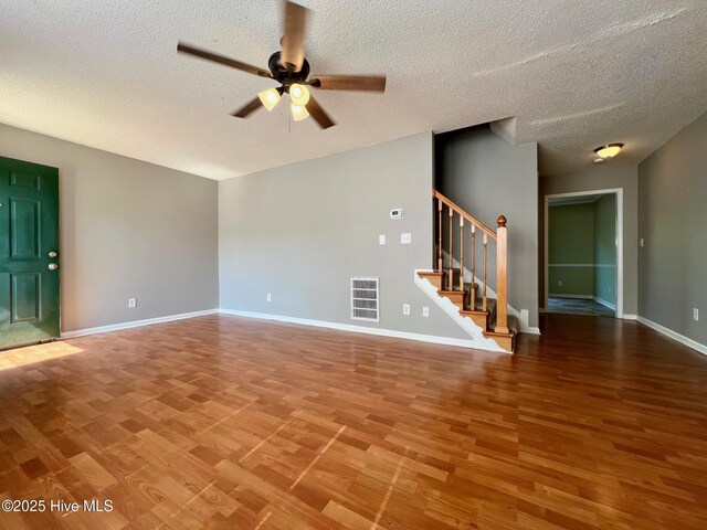 unfurnished living room featuring wood finished floors, a ceiling fan, stairs, a textured ceiling, and baseboards