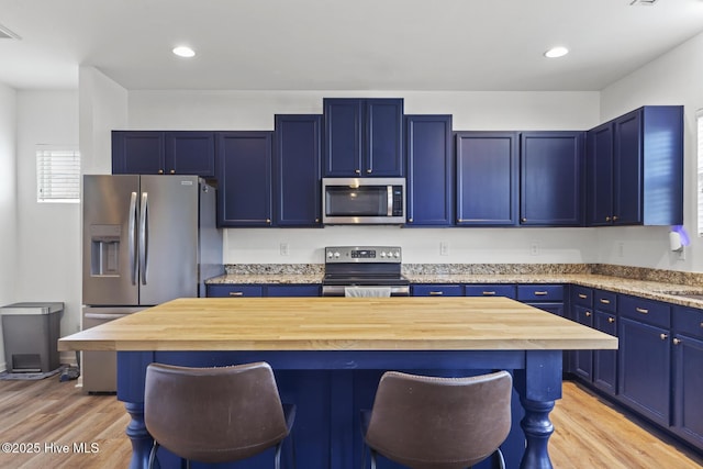 kitchen with appliances with stainless steel finishes, a breakfast bar area, wooden counters, and blue cabinets