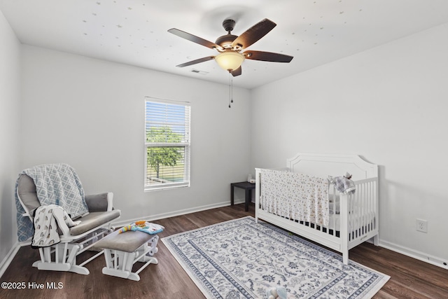 bedroom with a nursery area, a ceiling fan, baseboards, wood finished floors, and visible vents