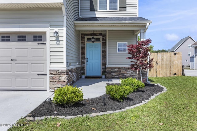 property entrance with a lawn, fence, covered porch, stone siding, and an attached garage