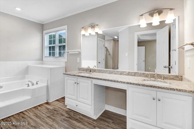 full bath featuring a sink, double vanity, a garden tub, and wood finished floors