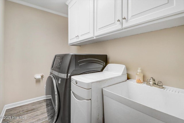 laundry room featuring washing machine and clothes dryer, cabinet space, a sink, baseboards, and wood finished floors