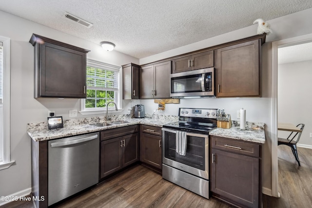 kitchen with visible vents, appliances with stainless steel finishes, dark brown cabinets, a sink, and dark wood-style floors