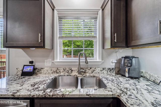 kitchen featuring light stone counters, a sink, dishwasher, and dark brown cabinets
