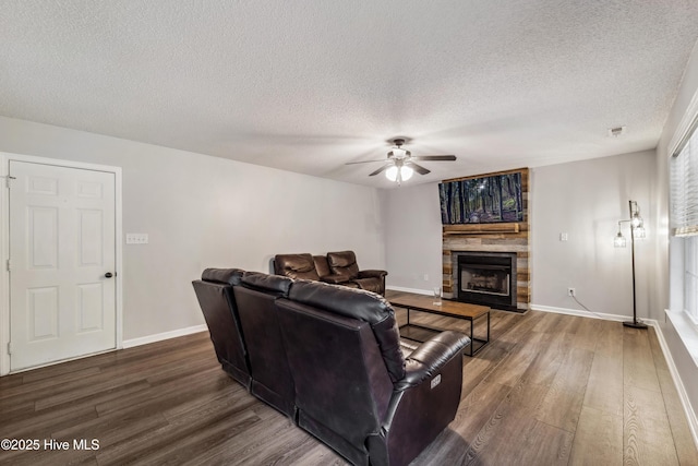 living area with a ceiling fan, a textured ceiling, dark wood finished floors, and a stone fireplace