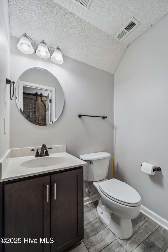 half bathroom with visible vents, vanity, toilet, baseboards, and a textured ceiling