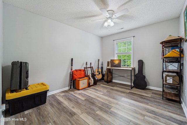 misc room with ceiling fan, a textured ceiling, visible vents, wood finished floors, and baseboards