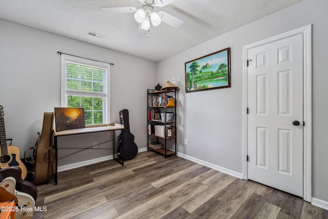 office area featuring a textured ceiling, a ceiling fan, baseboards, wood finished floors, and visible vents