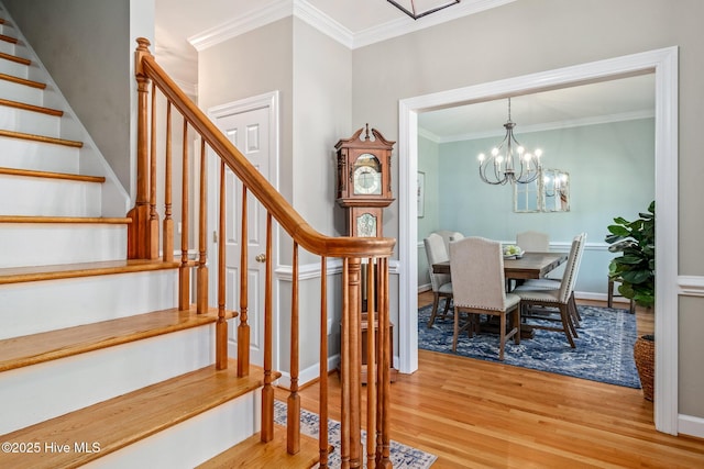 stairs with crown molding, wood finished floors, baseboards, and a notable chandelier