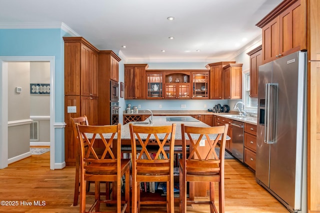 kitchen featuring brown cabinetry, a kitchen island with sink, crown molding, light countertops, and appliances with stainless steel finishes