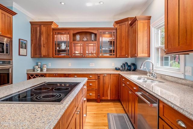 kitchen featuring light wood-style flooring, a sink, brown cabinetry, appliances with stainless steel finishes, and light stone counters