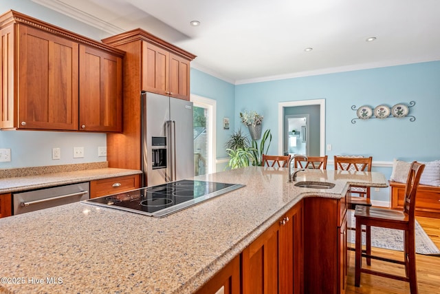 kitchen featuring a sink, stainless steel appliances, brown cabinets, crown molding, and a kitchen bar