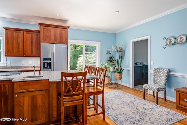kitchen featuring a sink, light stone counters, brown cabinetry, and stainless steel refrigerator with ice dispenser