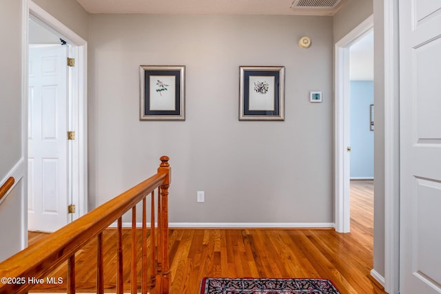 hallway featuring visible vents, baseboards, an upstairs landing, and light wood-style floors
