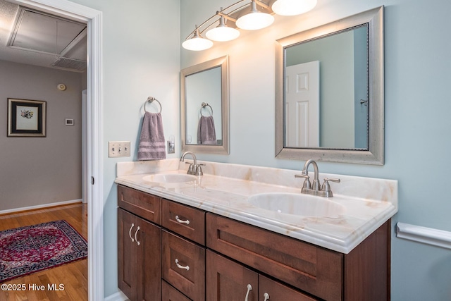 full bath featuring double vanity, wood finished floors, baseboards, and a sink