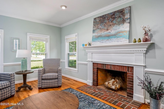 sitting room with baseboards, a brick fireplace, crown molding, and wood finished floors