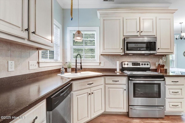 kitchen featuring dark countertops, hanging light fixtures, appliances with stainless steel finishes, a sink, and ornamental molding