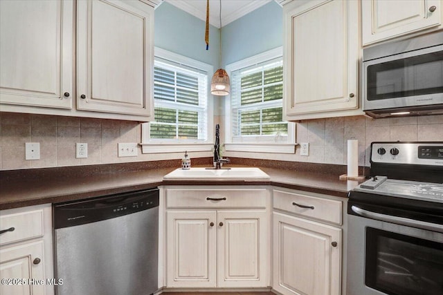 kitchen with stainless steel appliances, dark countertops, ornamental molding, and a sink