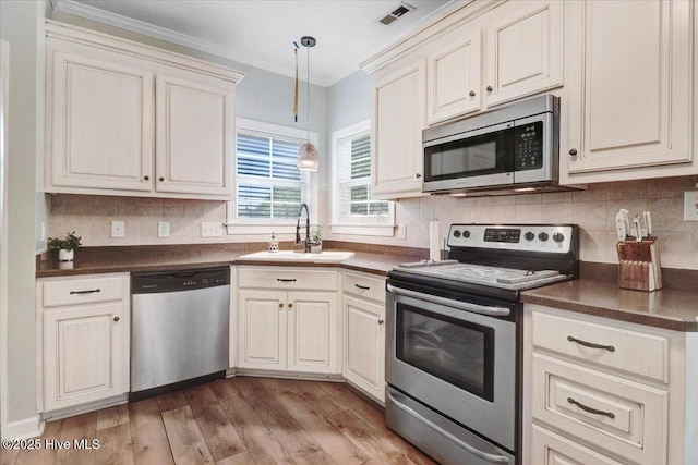kitchen featuring visible vents, appliances with stainless steel finishes, dark countertops, wood finished floors, and a sink