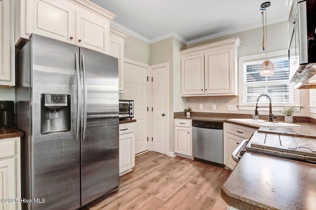 kitchen featuring crown molding, dark countertops, light wood-type flooring, appliances with stainless steel finishes, and hanging light fixtures