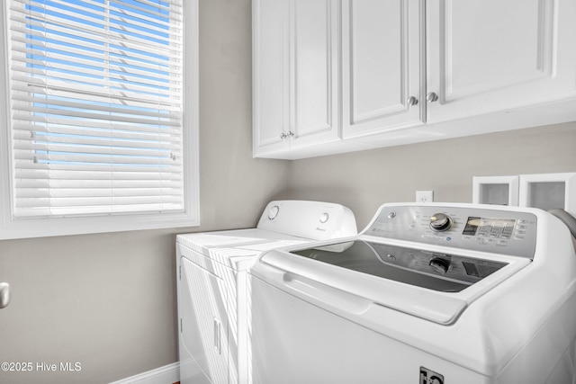 clothes washing area with baseboards, washer and clothes dryer, cabinet space, and a healthy amount of sunlight