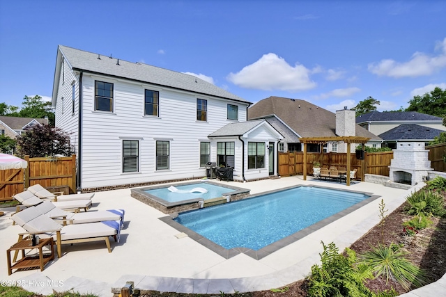 rear view of house with a pool with connected hot tub, a patio, a fireplace, and a fenced backyard
